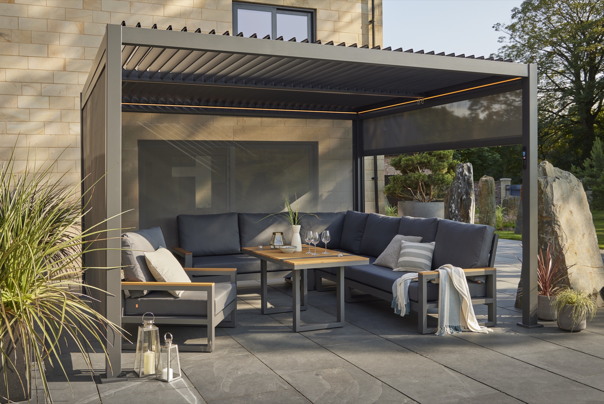 Aluminium pergola installed on a stone patio in daylight, with seating beneath